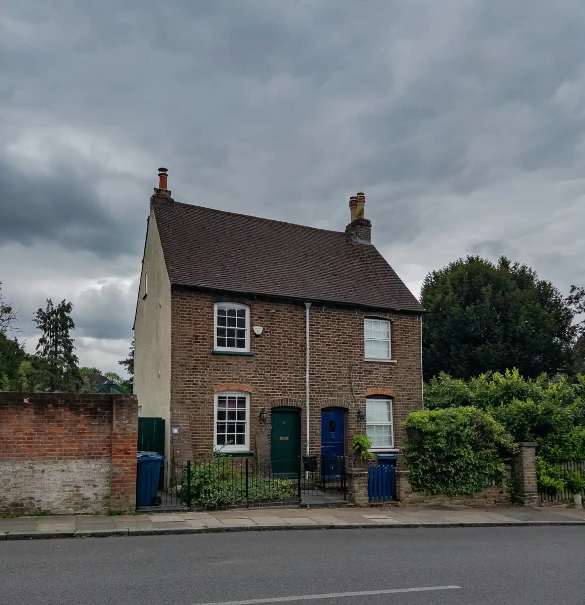 A pair of brick semi-detached cottages in Harrow on the Hill with a gable end wall, a dark tiled roof, two chimney stacks and a cloudy sky; the vertical gable is the shape a hip to gable conversion creates