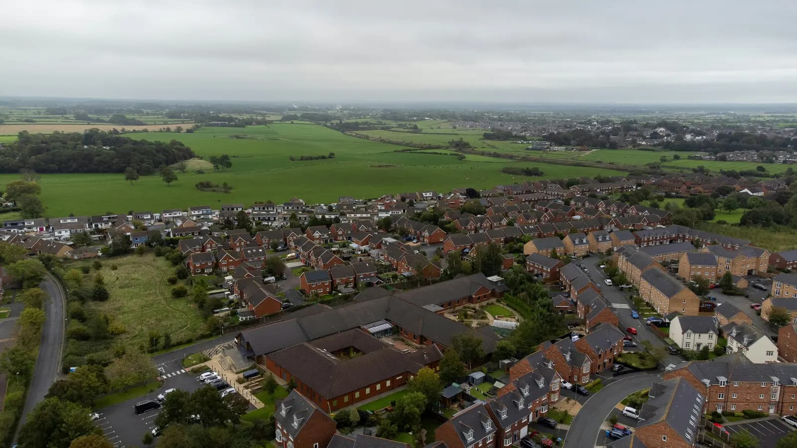 Aerial view of a brick housing estate in Wesham near Preston, Lancashire, with many semi-detached and terraced houses under hipped slate-grey roofs and fields beyond