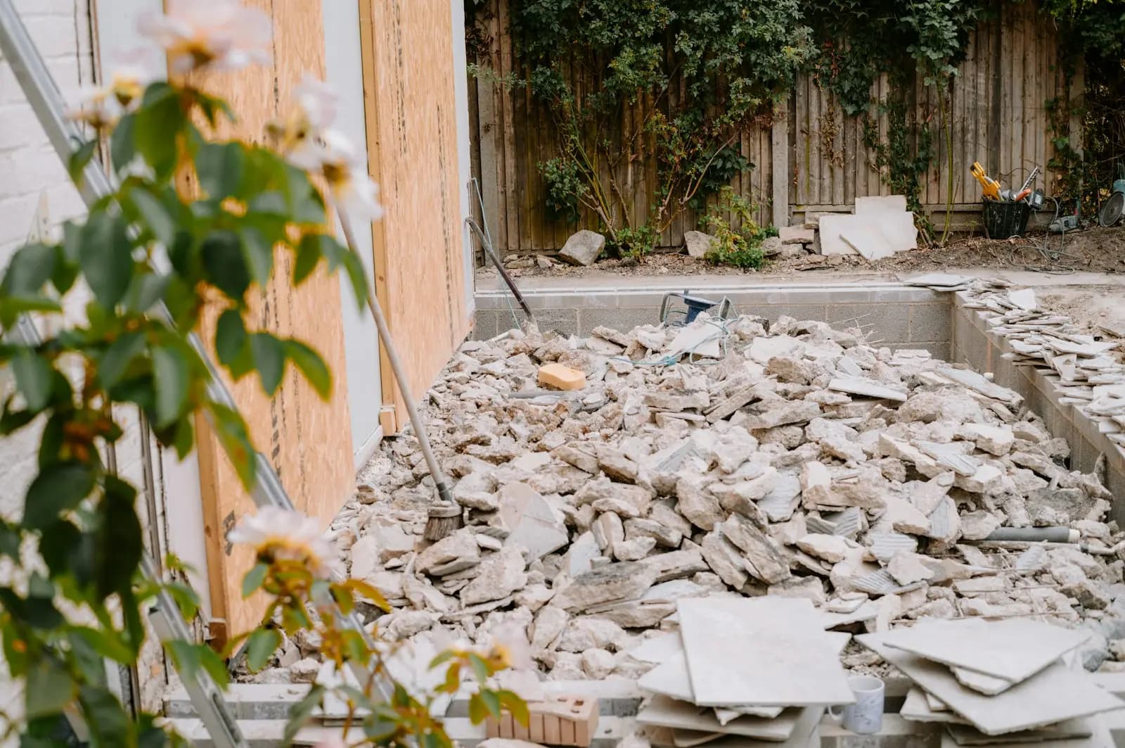 A rear garden extension under construction: blockwork foundation walls filled with broken concrete and paving, timber sheathing on the house wall and a lapped fence behind
