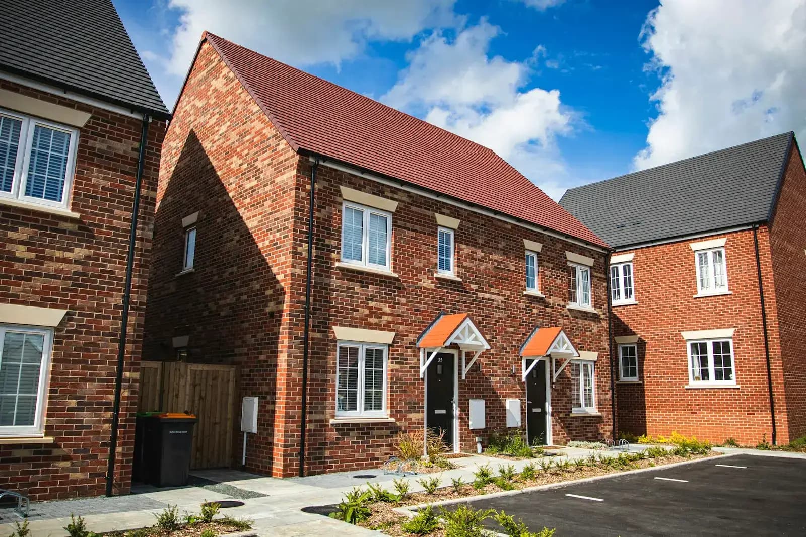 Red-brick semi-detached houses with tiled roofs and white-framed windows on a new residential street in Bedford, England