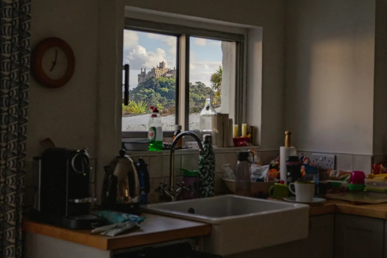 A lived-in kitchen in Marazion, Cornwall, with a ceramic Belfast sink, mixer tap, wooden worktops and a UK double socket, and St Michael's Mount visible through the window