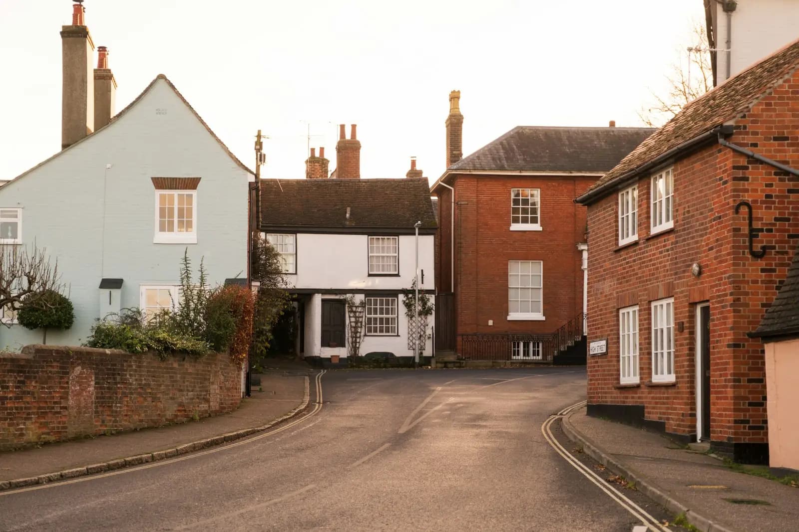 A curving residential street in Manningtree with a pale blue gabled house, a white timber-framed cottage and red brick houses with white windows and chimneys