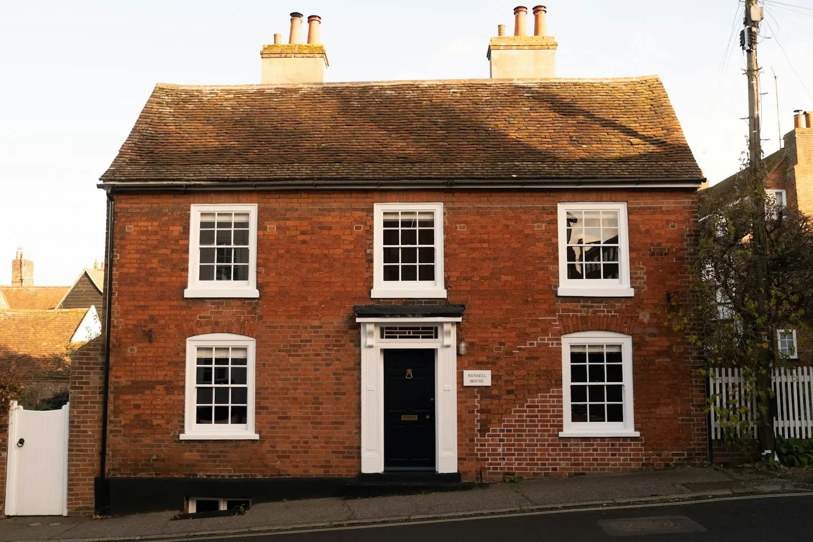 A two-storey red brick Georgian-style house with white sash windows, a dark blue front door and two tall chimney stacks, seen from the street in Manningtree, Essex