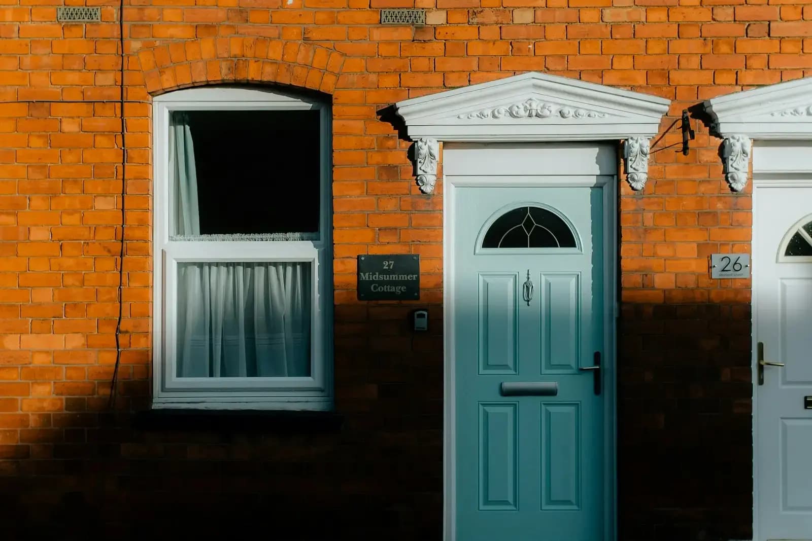 The front of a Victorian-style red brick terraced house in Stratford-upon-Avon, with an arched sash window, a pale blue panelled door with a decorative pediment, and a neighbouring door to the right