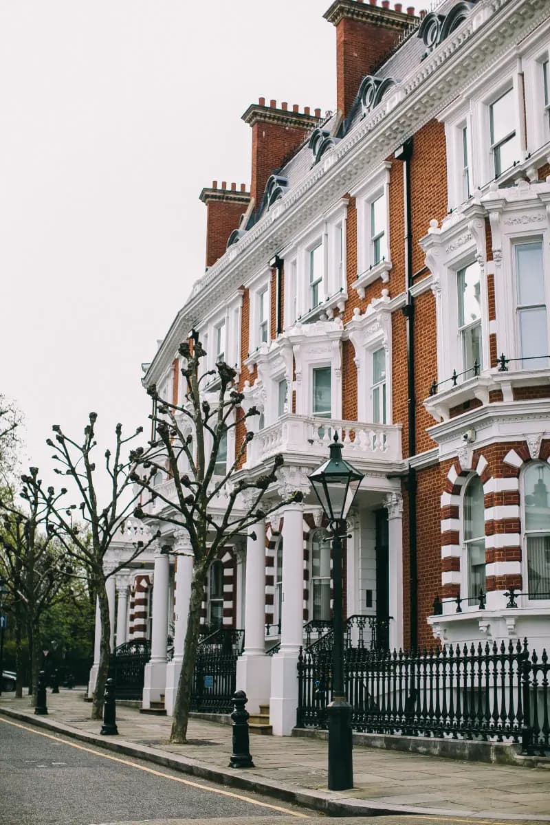 A curved terrace of tall red-brick and white-stucco Victorian houses on a quiet London street, with chimney stacks, dormer windows and black iron railings