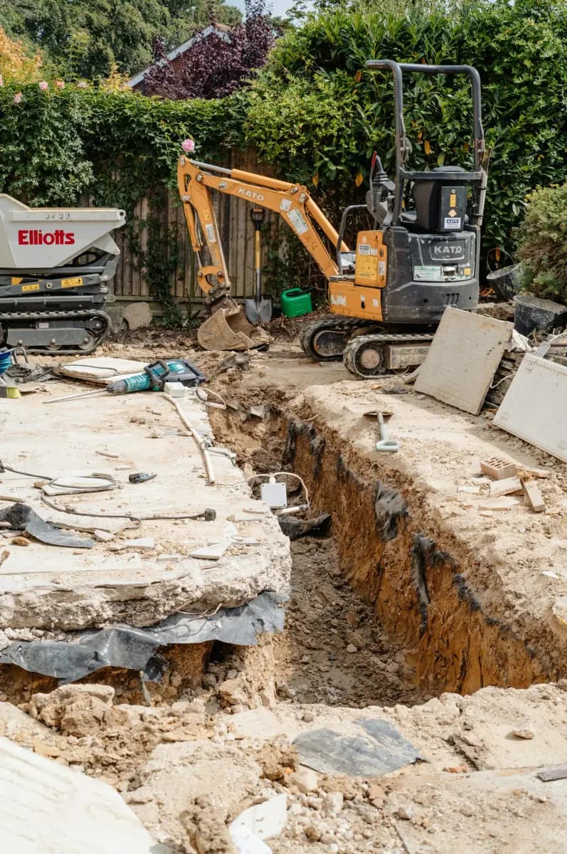 A mini excavator digging a trench in a residential site, with spoil heaped beside the trench