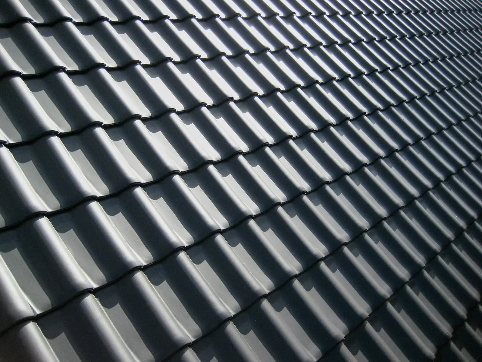 Close-up of dark grey interlocking roof tiles in bright sunlight, casting sharp parallel shadows
